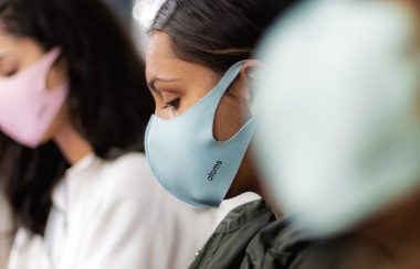 Three people wearing medical masks outdoors. Masks are pink, blue and white.