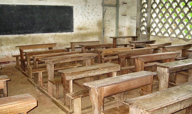 Salle de classe au cameroun avec plusieurs pupitres en bois et un tableau à craies installé sur le mur.