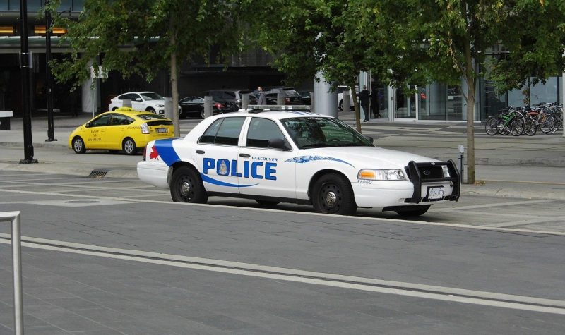 Route au premier plan et au second une voiture de police blanche et bleu et en arrière plan des arbres et une voiture de taxi jaune