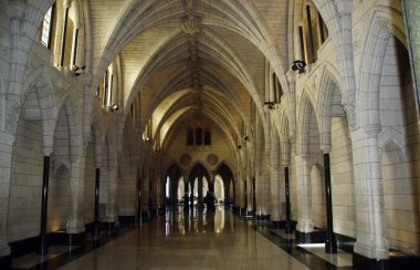 A hallway in parliament in Ottawa. The ceiling is an arch shape, with light stone columns along the walls.
