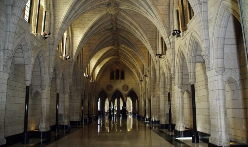 A hallway in parliament in Ottawa. The ceiling is an arch shape, with light stone columns along the walls.