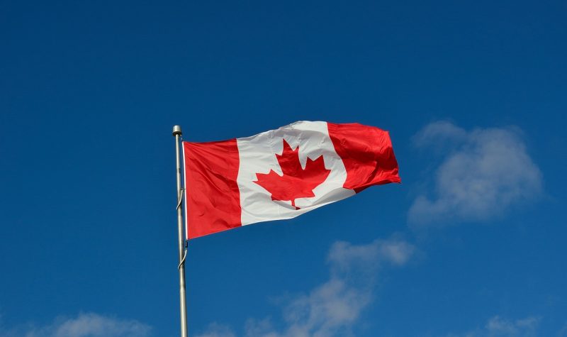 A Canadian flag blowing in the wind. Blue skies surround the flag.