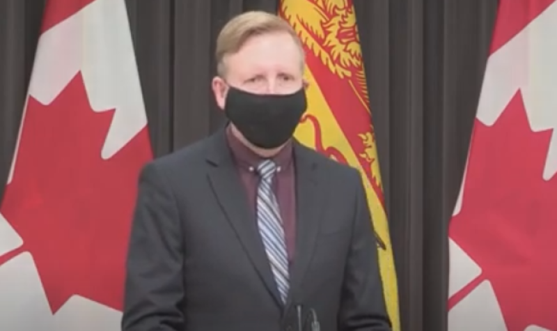 Dominic Cardy portant un masque noir devant un drapeau néo-brunswickois et canadien