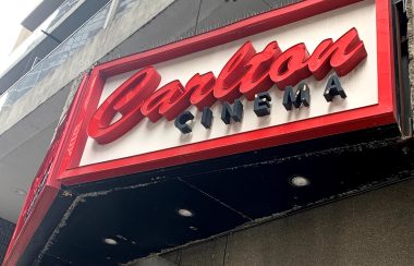 Red and black letters on a white sign on an elevated wall outside.