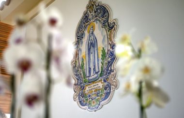 Gravure en mozaïk de la vierge Marie sur un mur avec deux gerbes de fleurs posées devant.