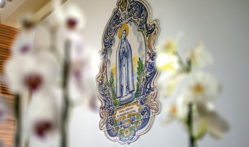Gravure en mozaïk de la vierge Marie sur un mur avec deux gerbes de fleurs posées devant.