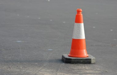 An orange and white reflective traffic cone sits on a paved asphalt road.