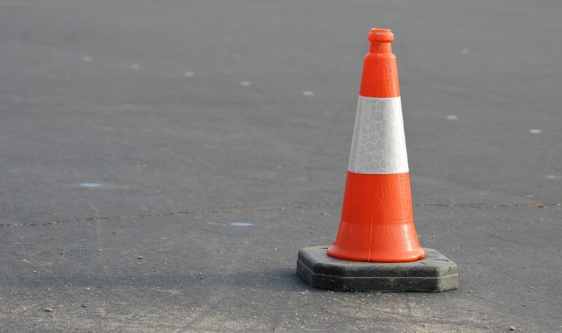 An orange and white reflective traffic cone sits on a paved asphalt road.