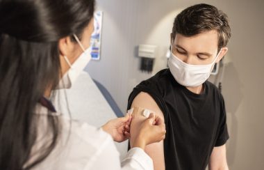 A boy receiving a bandaid on his arm from a medical worker.