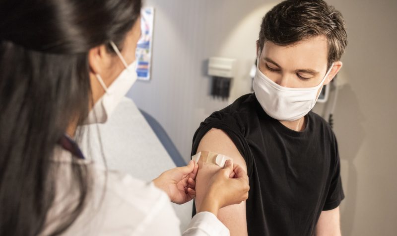 A boy receiving a bandaid on his arm from a medical worker.