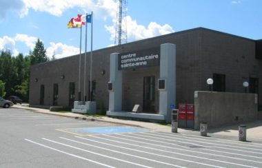 bâtiment du centre communautaire Sainte-Anne dans lequel l'école est installée de Fredericton, les drapeaux du Nouveau-Brunswick, de l'Acadie et du Canada flottent devant.