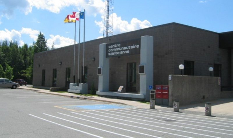 bâtiment du centre communautaire Sainte-Anne dans lequel l'école est installée de Fredericton, les drapeaux du Nouveau-Brunswick, de l'Acadie et du Canada flottent devant.