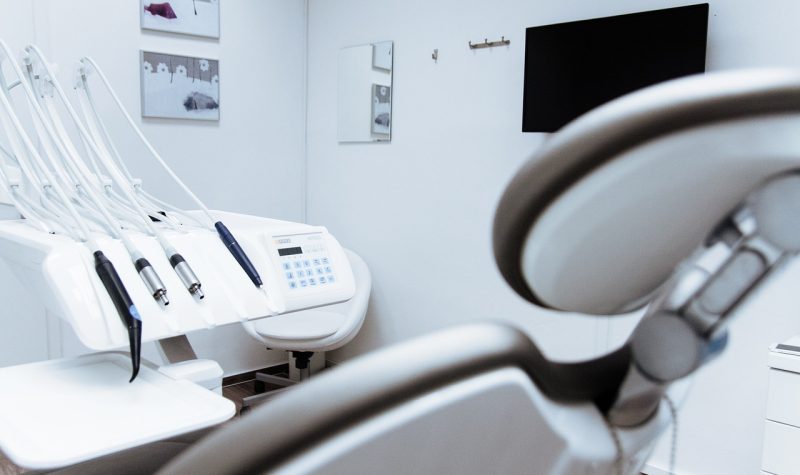 Une chaise de dentiste vide se trouve au premier plan d'une salle blanche épurée