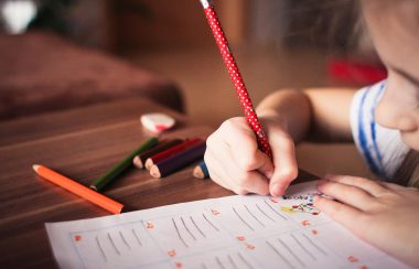 Un enfant tient un crayon et répond à des questions sur une feuille de papier.