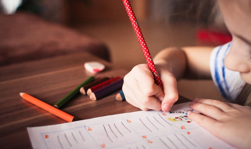 Un enfant tient un crayon et répond à des questions sur une feuille de papier.