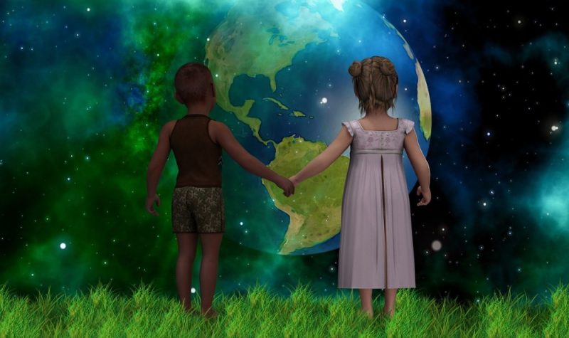 Deux enfants debout sur l'herbe se tiennent la main devant un fond de planète terre dans l'univers.