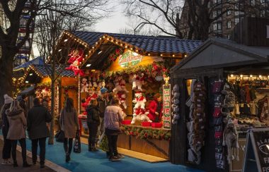 Chalet de marché de Noël éclairé avec des passants et ou clients devant la structure.