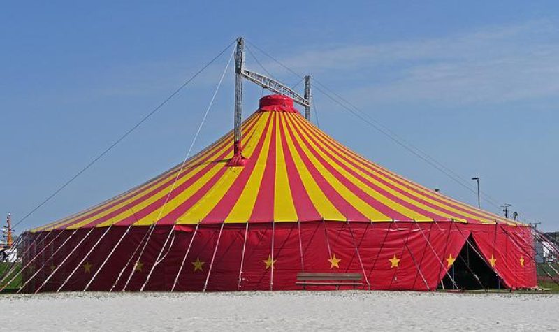 Tente de cirque rouge et jaune. Le toit de la tente est composé de lignes rouges et jaunes. Le contour de la tente est rouge avec des étoiles jaunes.