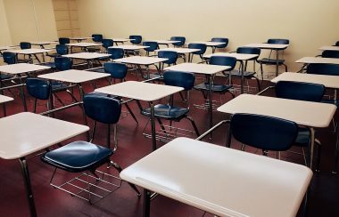 Des rangées de pupitres dans une salle de classe vide.