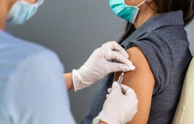 Patiente portant un polo gris se fait vacciner par une infirmière qui porte des gants blancs.
