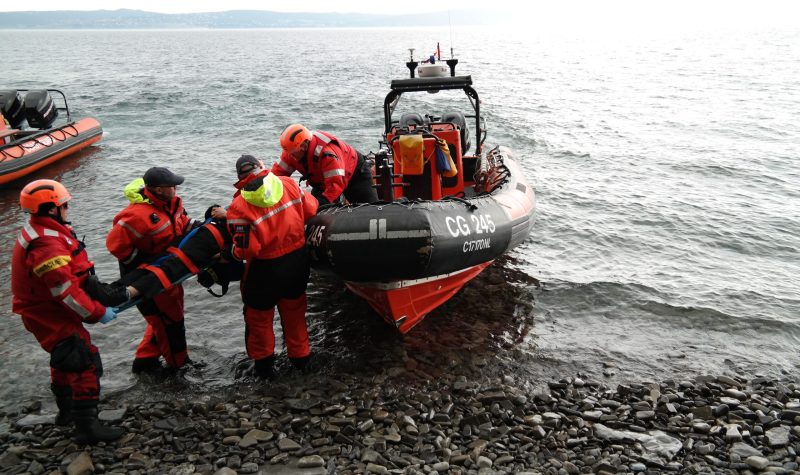 Three coast guard are training how to safely lift someone on a stretcher onto a rigid hull inflatable boat.