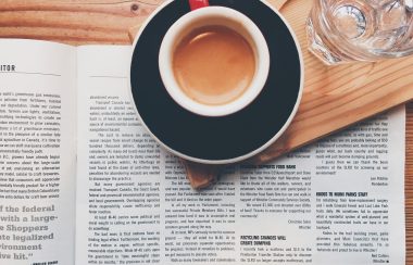 A cup of coffee is set over an open newspaper.