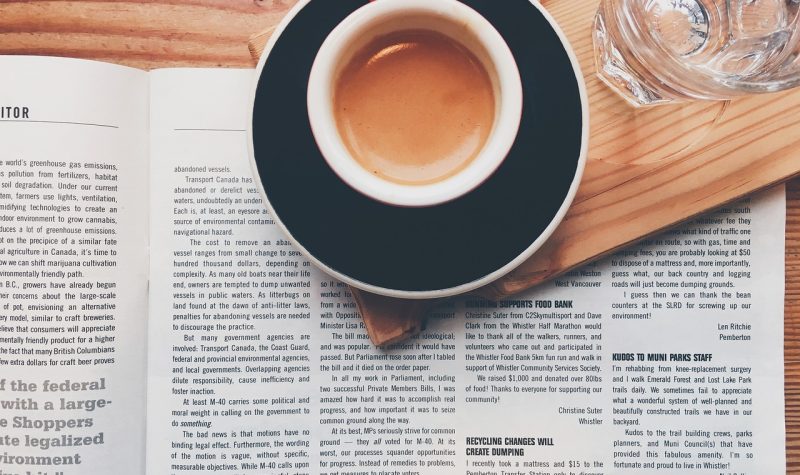 A cup of coffee is set over an open newspaper.