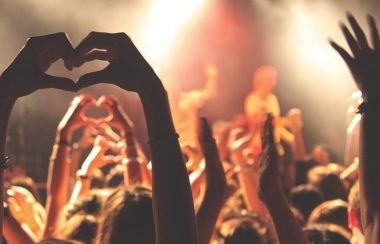 Une photo d'un concert, avec quelqu'un qui fait un signe du cœur avec ses mains.
