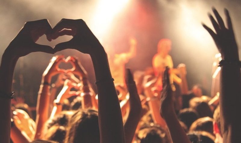 Une photo d'un concert, avec quelqu'un qui fait un signe du cœur avec ses mains.