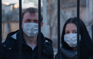 Un homme et une femme derrière des grilles portant un masque