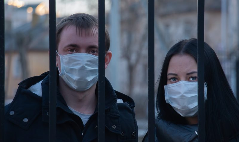 Un homme et une femme derrière des grilles portant un masque
