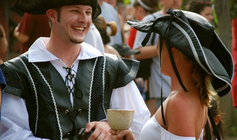 On voit un couple costumé en pirates lors d'une fête thématique. Les deux portes des vêtements anciens et un chapeau d'époque. À l'arrière on peut voir d'autre personnes participants à l'activité qui ne sont pas costumés