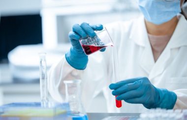 Une scientifique en uniforme effectue une analyse sanguine en versant un échantillon dans une éprouvette.