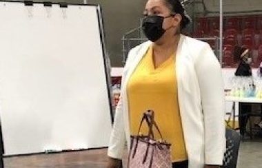 First Nations lady wearing white and yellow shirt with mask talking about treaties and culture