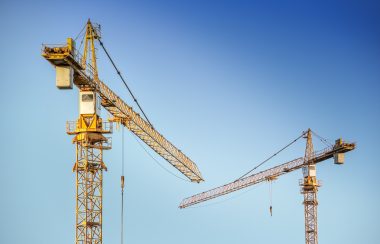 Deux grues de chantiers sur un ciel bleu. les grues sont jaunes