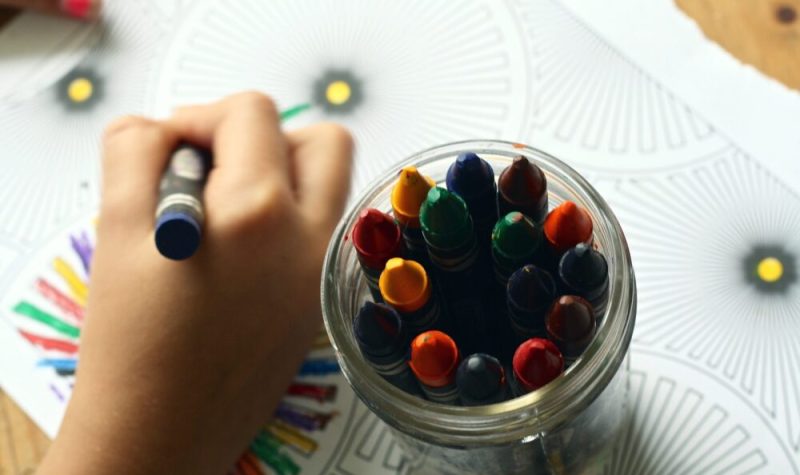 Une main d'enfant, un bol de couleurs et des papiers.