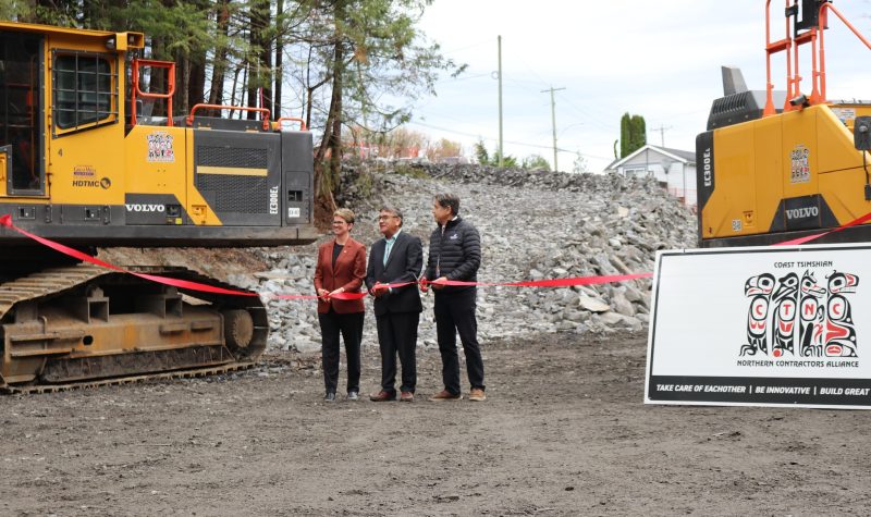 One woman and two men standing on construction site holding ribbon