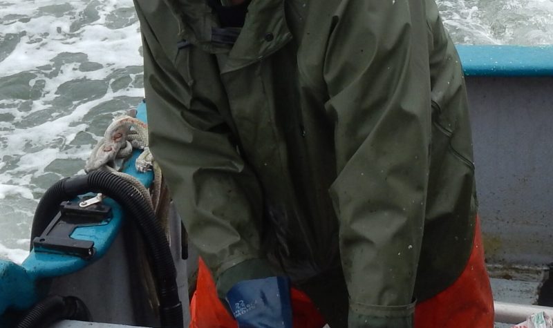 Charles Menzies stands on a boat gutting a fish with a smile on his face