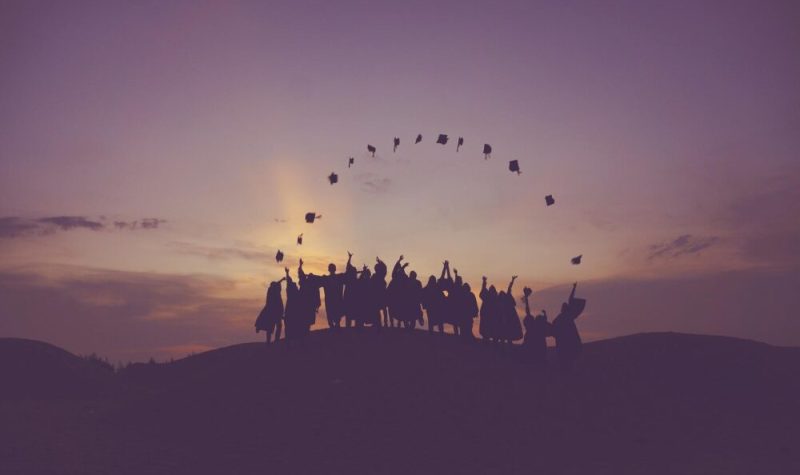 Les silhouettes d'un groupe à l'horizon lancent leurs chapeaux de diplômés dans l'air.