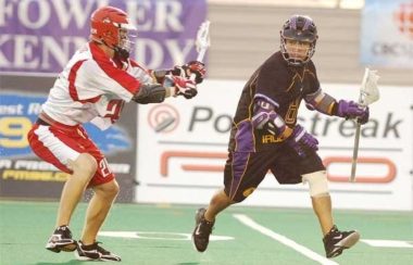 Two men playing field lacrosse. A man in the black uniform carries the ball against a man in a red and white uniform.