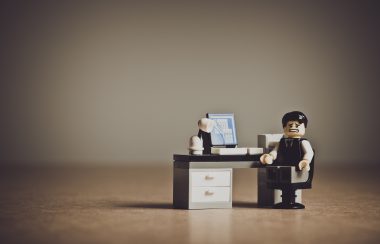 Un playmobile assis derrière un bureau fait la grimace derrière son écran d'ordinateur.