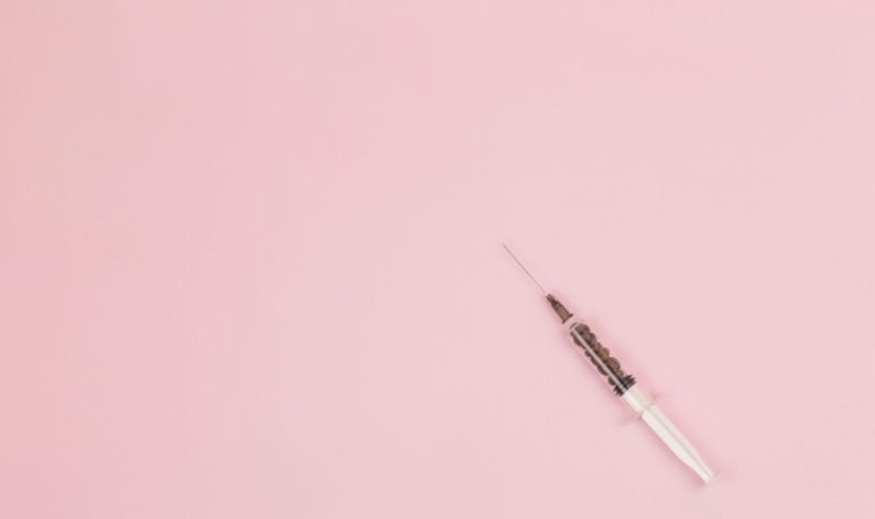 A single syringe sits on a pink background.