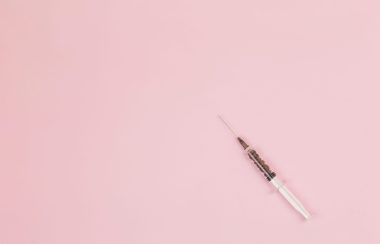 A single syringe against a pink background.