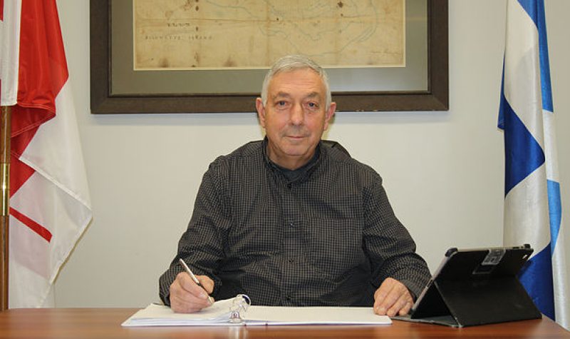 Chichester Mayor Donald Gagnon, seated at a desk in between a Canadian and Quebec flag. wearing a dark collared shirt.