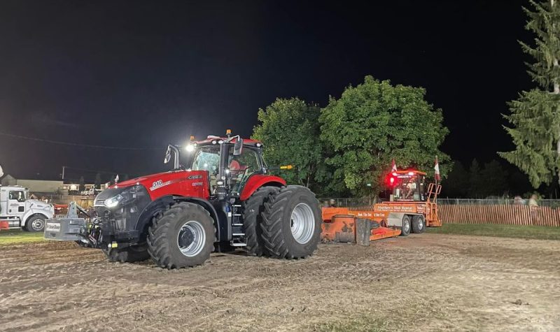A tractor pull takes place in a rural landscape under a night sky.