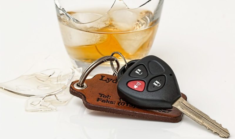 On peut voir une photo rapproché d'un verre d'alcool brisé posé prêt de clé de voiture. Des morceau de verres sont également visibles. La photo a été prise sur un fond blanc.