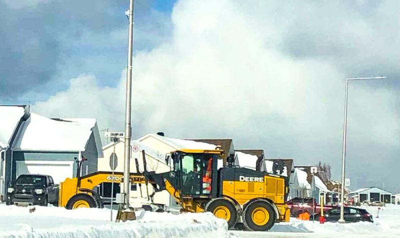 Une déneigeuse jaune déblaie le coin d'une rue