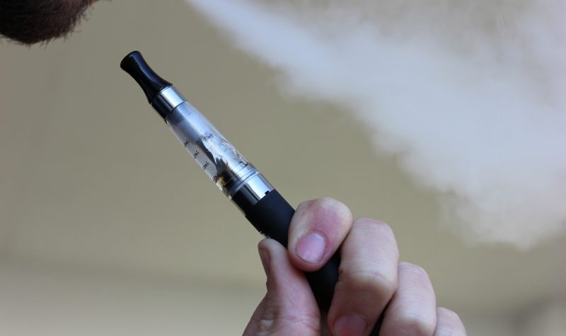 A black and white vape pen being smoked by a man.