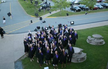 Une foule d'étudiants lancent leur chapeau à l'extérieur