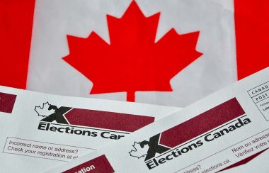 A Canadian flag sits behind the top of two voting ballots for Elections Canada